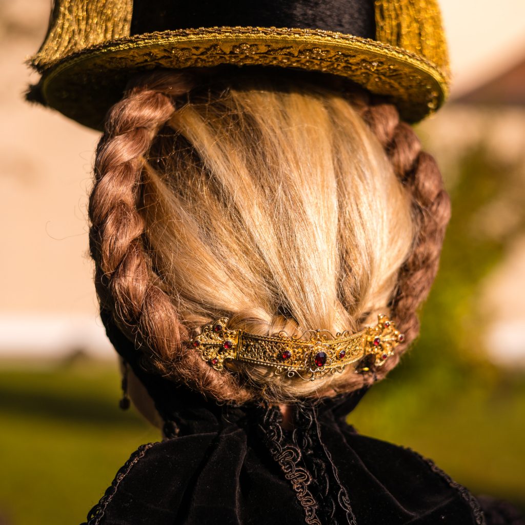 Röckifrau mit Gretl-Frisur, geschmückt mit filigraner, granatbesetzter Goldspange. Sie trägt den sog. Priener Hut, hier in einer Variante mit vier Goldquasten (beidseitiges Quastenpaar).